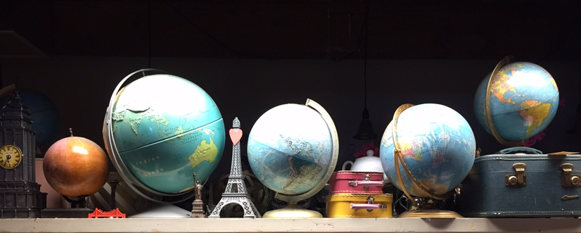 Globes of the world on a table with travel-related items, like an Eiffel Tower and a suitcase.