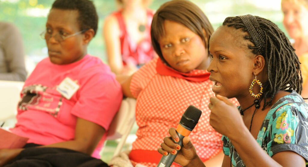 A disabled woman speaks into a microphone as others listen.