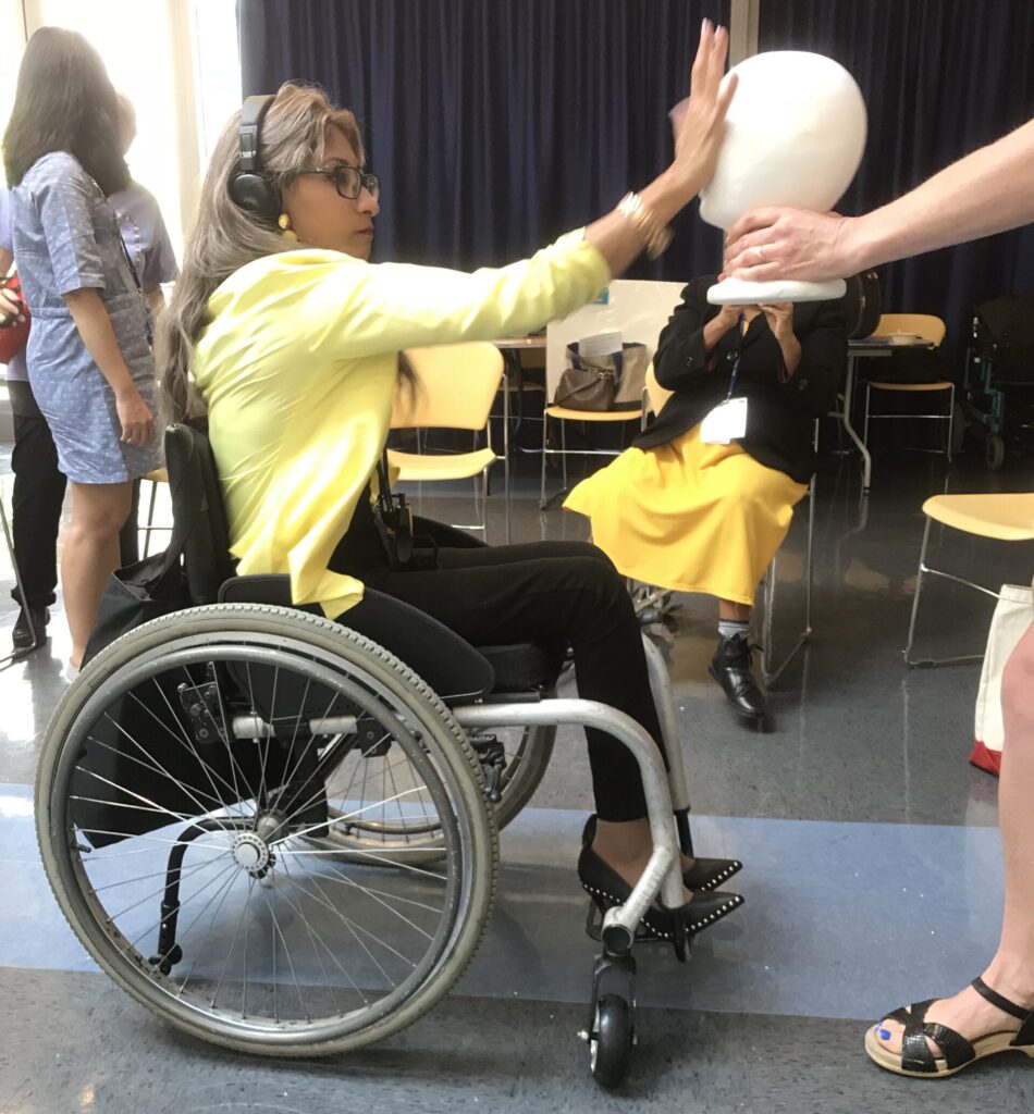 Woman using a wheelchair extending her arm while practicing self defense on a mannequin head.