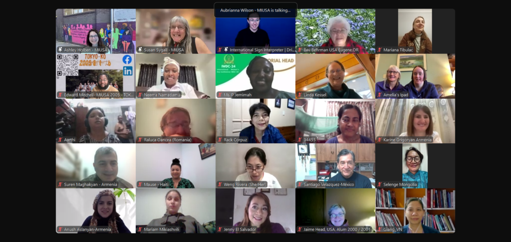 Zoom screenshot of 25 individual videos showing the faces of smiling MIUSA staff and alumni from around the world. Susan Sygall is pictured.