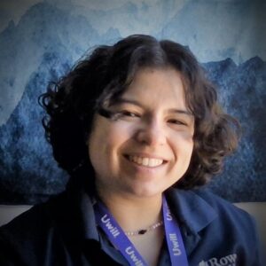 White woman with short, dark curly hair smiling.