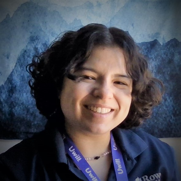 White woman with short, dark curly hair smiling.