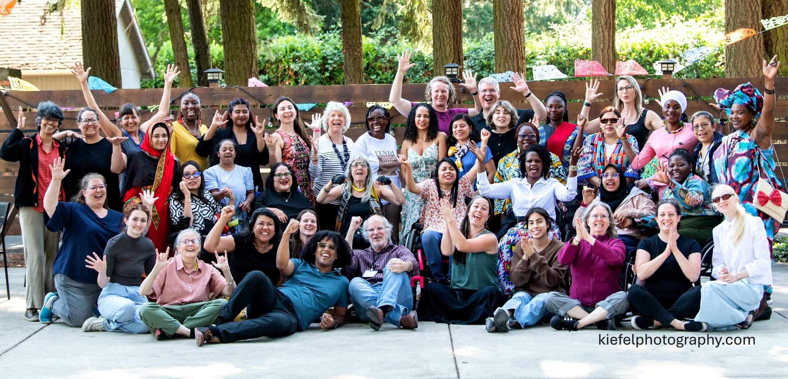 Large group of women of diverse races and disabilities, gathered in a group outdoors.