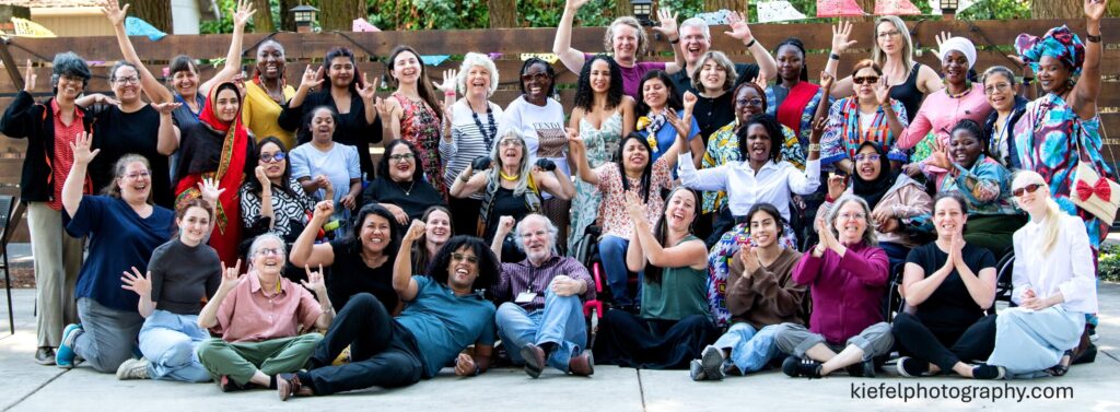 Vibrant photo of the WILD delegation, staff and interpreters and GDDI professionals waving hands in an outdoor setting.