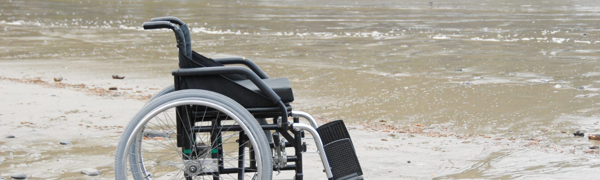 A manual wheelchair in the sand with ocean waves in the background.